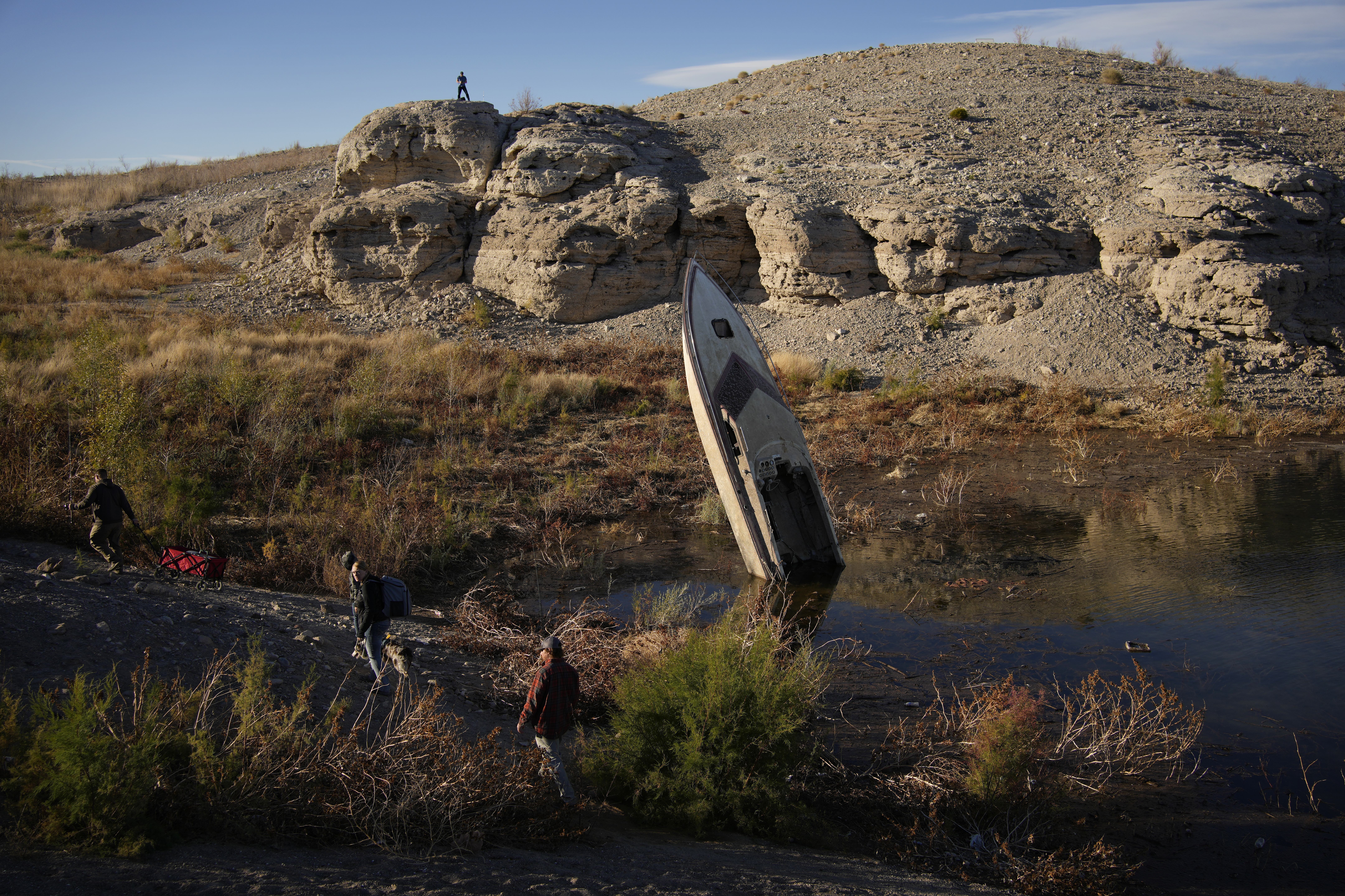 People walk by a formerly sunken boat standing upright into the air with its stern buried in the mud along the shoreline of Lake Mead. People walk by a formerly sunken boat standing upright into the air with its stern buried in the mud along the shoreline of Lake Mead.